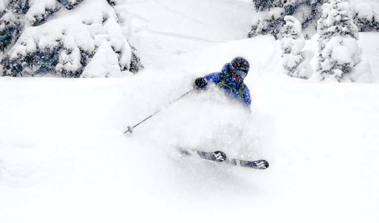 A photo of Lee Alston skiing, with snow bursting up in front of him.