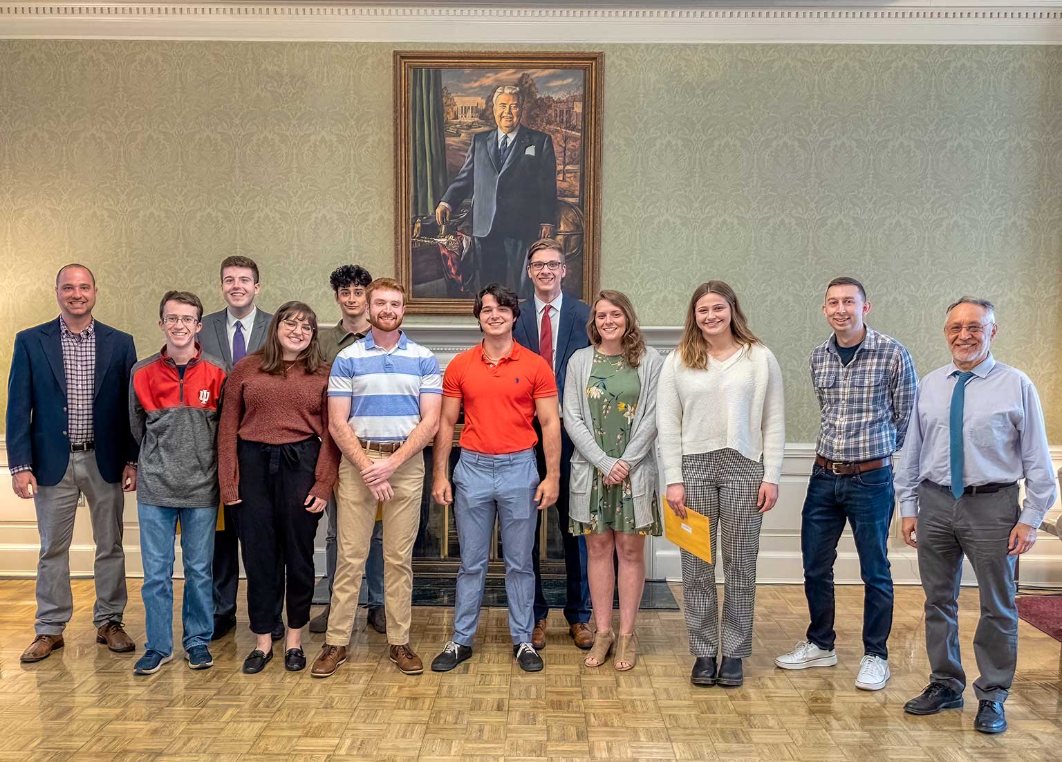 A group of undergraduate economics students pose in the Indiana Memorial Union, with a portrait of Herman B Wells above them.