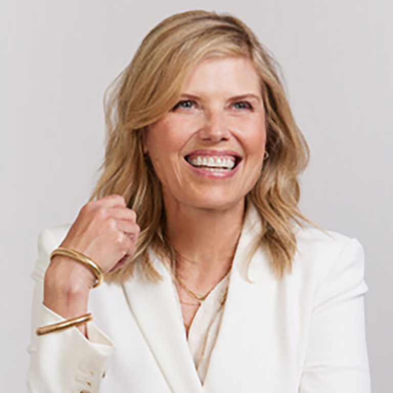 A headshot of alumna Tracy Gardner, who wears a bright white suit and poses against a beige background.
