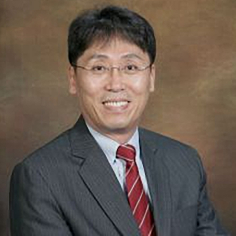 A headshot of Joon Park, who wears a brown suit and a red tie.