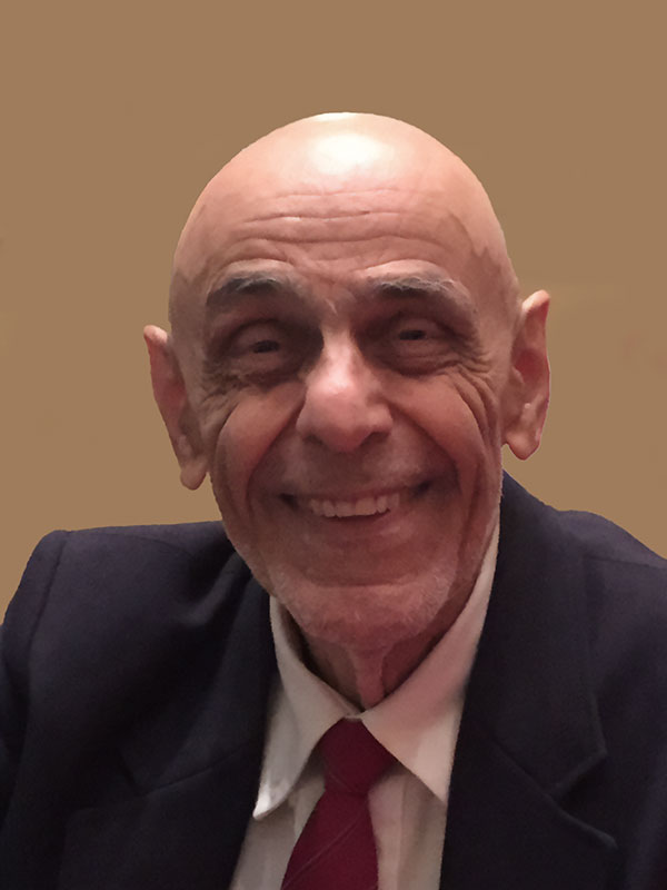 A headshot of Michael Ali Fekrat, who wears a dark blazer, white dress shirt, and red tie.