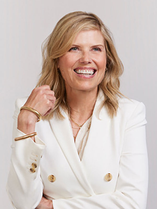 A headshot of Tracy Gardner, who wears a white suit and poses against a beige background.