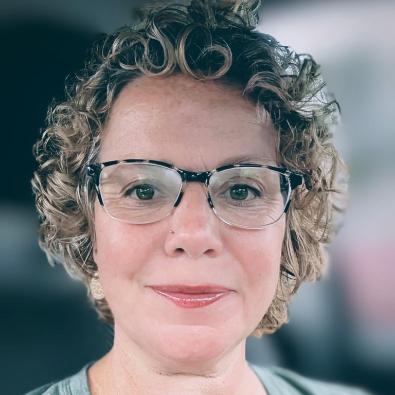 A headshot of Erin Kirchhofer, who wears plastic frame glasses and poses inside.